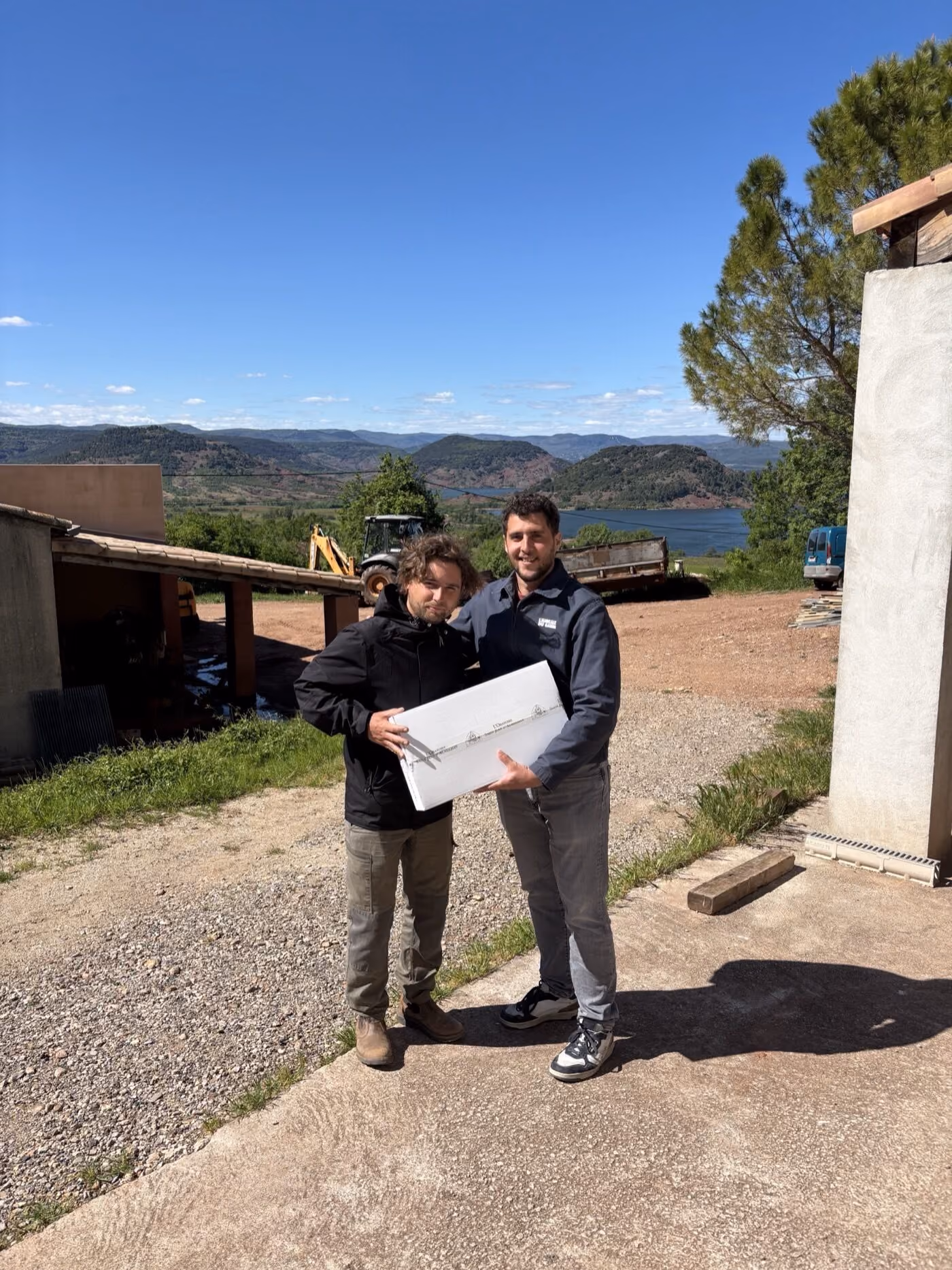 Guillaume et Florent posant avec un carton de L'Oratoire Saint Jean d'Aureilhan devant les collines et le lac du Salagou