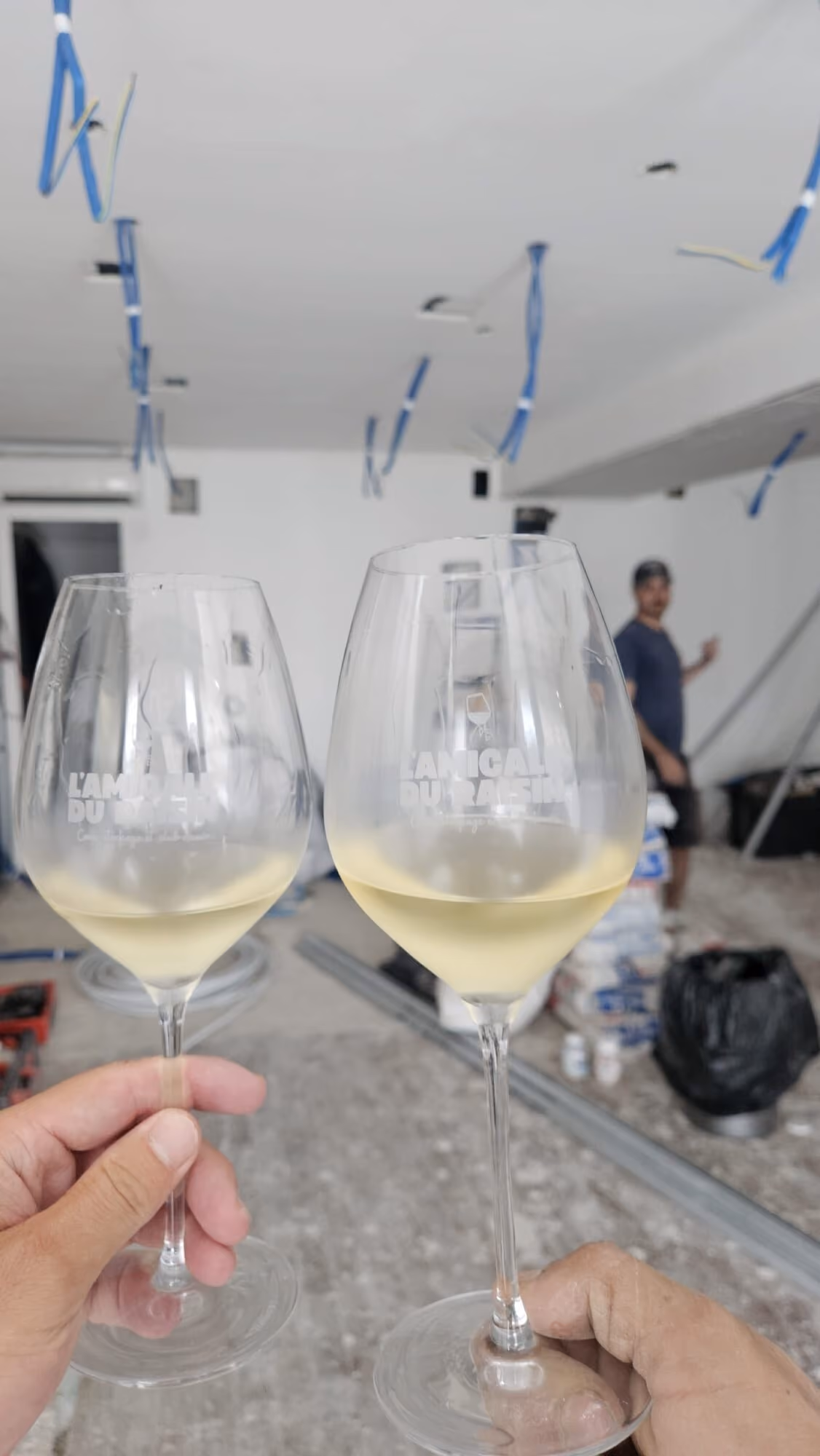 Deux verres gravés L'Amicale du Raisin levés en trinquant dans la future boutique en plein chantier