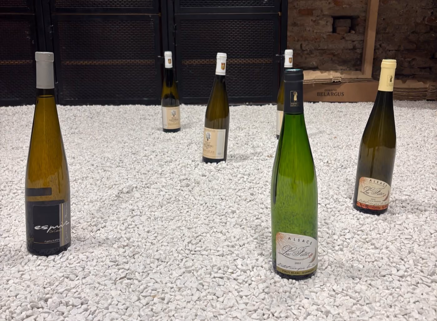 Les bouteilles de la dégustation Alsace : Luc Faller, Agathe Bursin et les Grands Crus Kientzler posés sur le gravier blanc de la cave